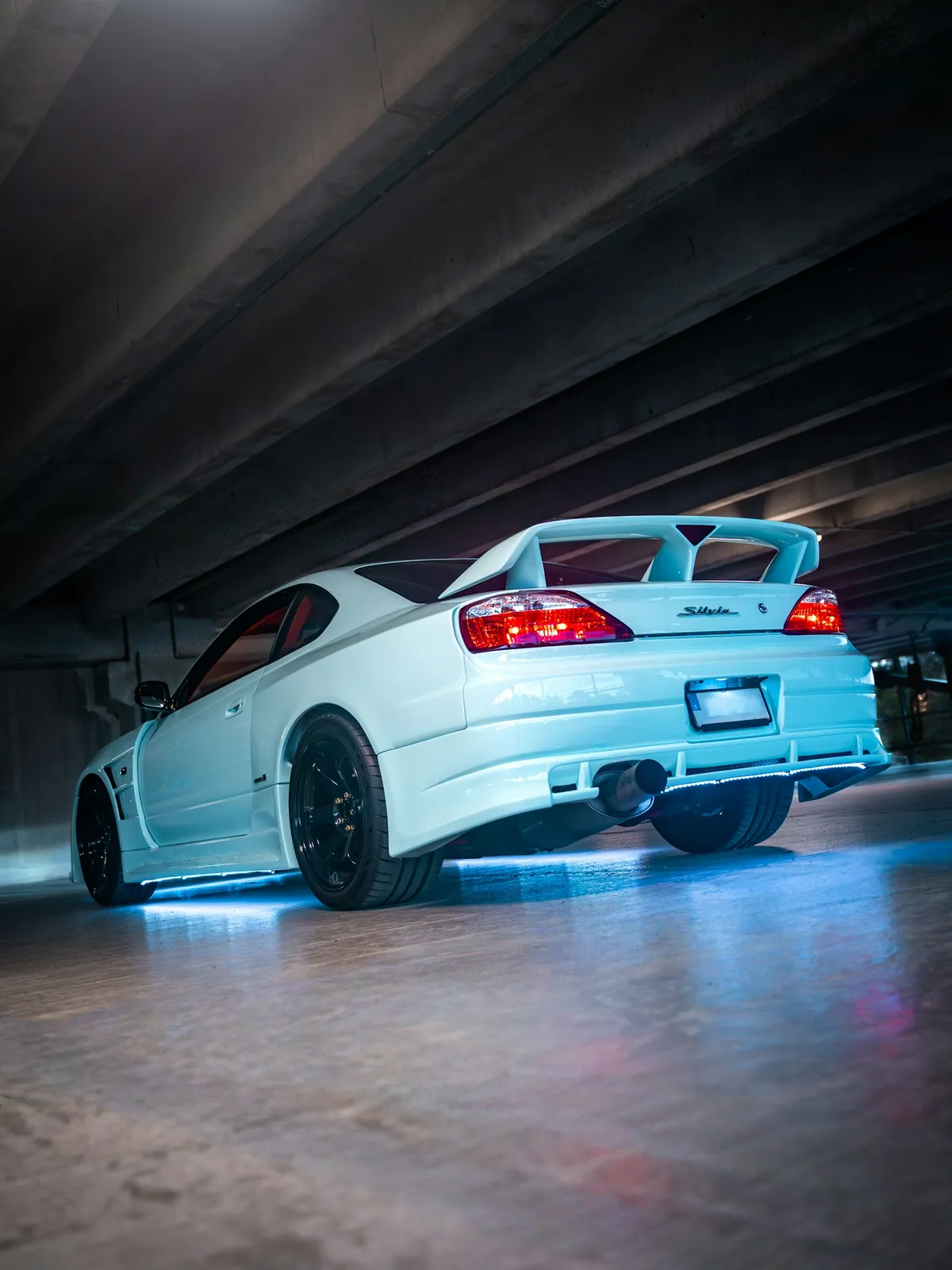 White sports car with blue underglow lighting the concrete floor of a parking garage