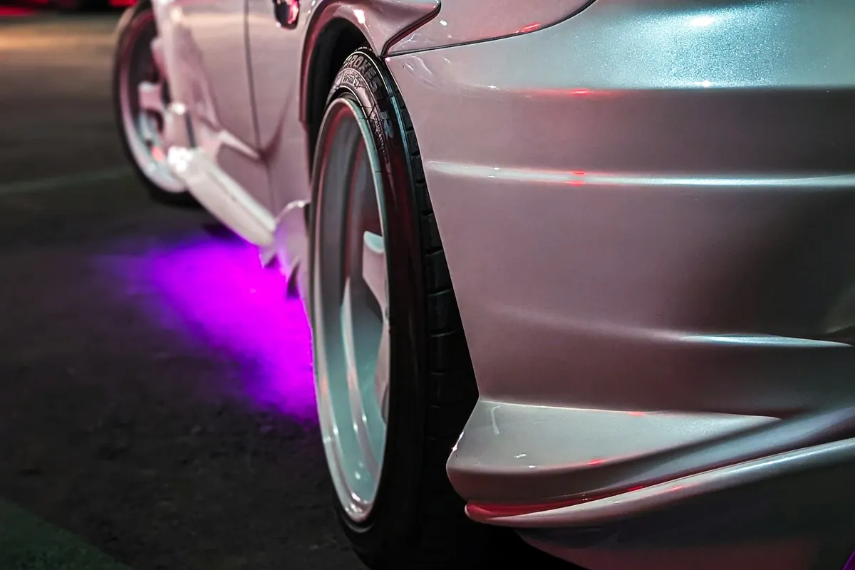 Purple underglow lighting the ground beside the rear wheel of a white sports car